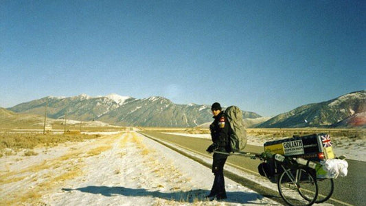 Karl Bushby walking with his distinctive yellow Goliath Expedition cart on empty mountain road, capturing the solitary nature of his 27-year around-the-world journey