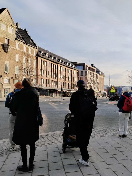Parents with backpacks pushing a stroller through a cobblestone square in a Nordic city, showcasing modern family urban exploration
