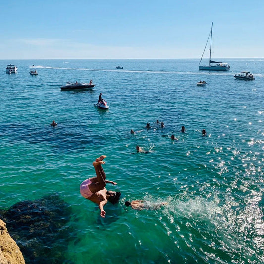Cliff jumping action shot showing person mid-air jumping into clear turquoise water with swimmers and boats demonstrating what cliff jumping feels like during the fall