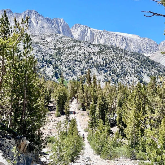 A well-marked hiking trail winds through rocky terrain toward dramatic mountain peaks, demonstrating proper trail navigation in high-altitude outdoor activities