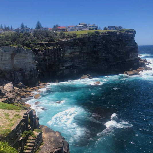 Beautiful cliff jumping destination with turquoise ocean waves crashing on rocks and coastal houses above showing why nature spots make cliff jumping more relaxing