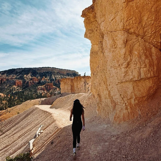 Female hiker walking through sandy canyon trail with rock walls, illustrating real-world lightweight backpack performance in desert hiking conditions