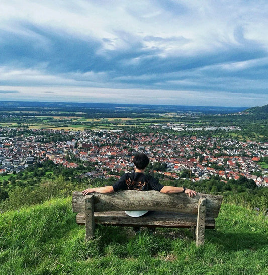 Person sitting on a wooden bench overlooking the town of Weilheim an der Teck from a grassy hillside