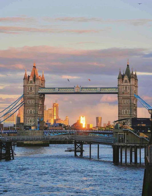 Tower Bridge in London at sunset with golden light reflecting off city buildings across the Thames