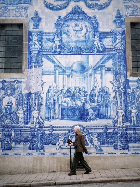 Elderly man walking past detailed blue azulejo tile wall in Porto, Portugal
