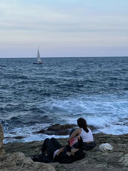 Solo traveler sitting by the sea with a compact expandable backpack, watching the waves