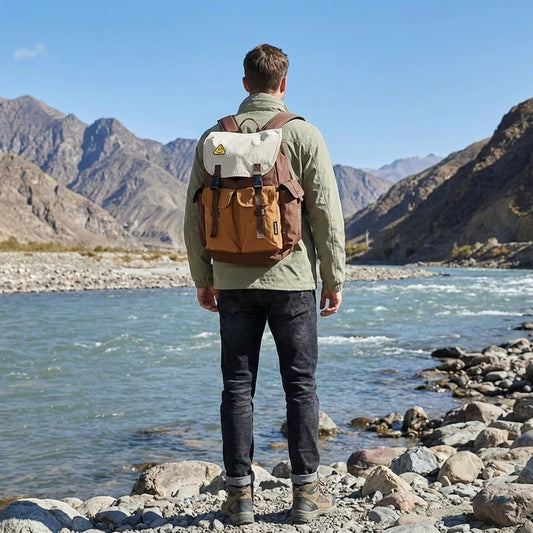 Back view of a traveler wearing the 7706 waterproof backpack while standing by a mountain river in an open valley