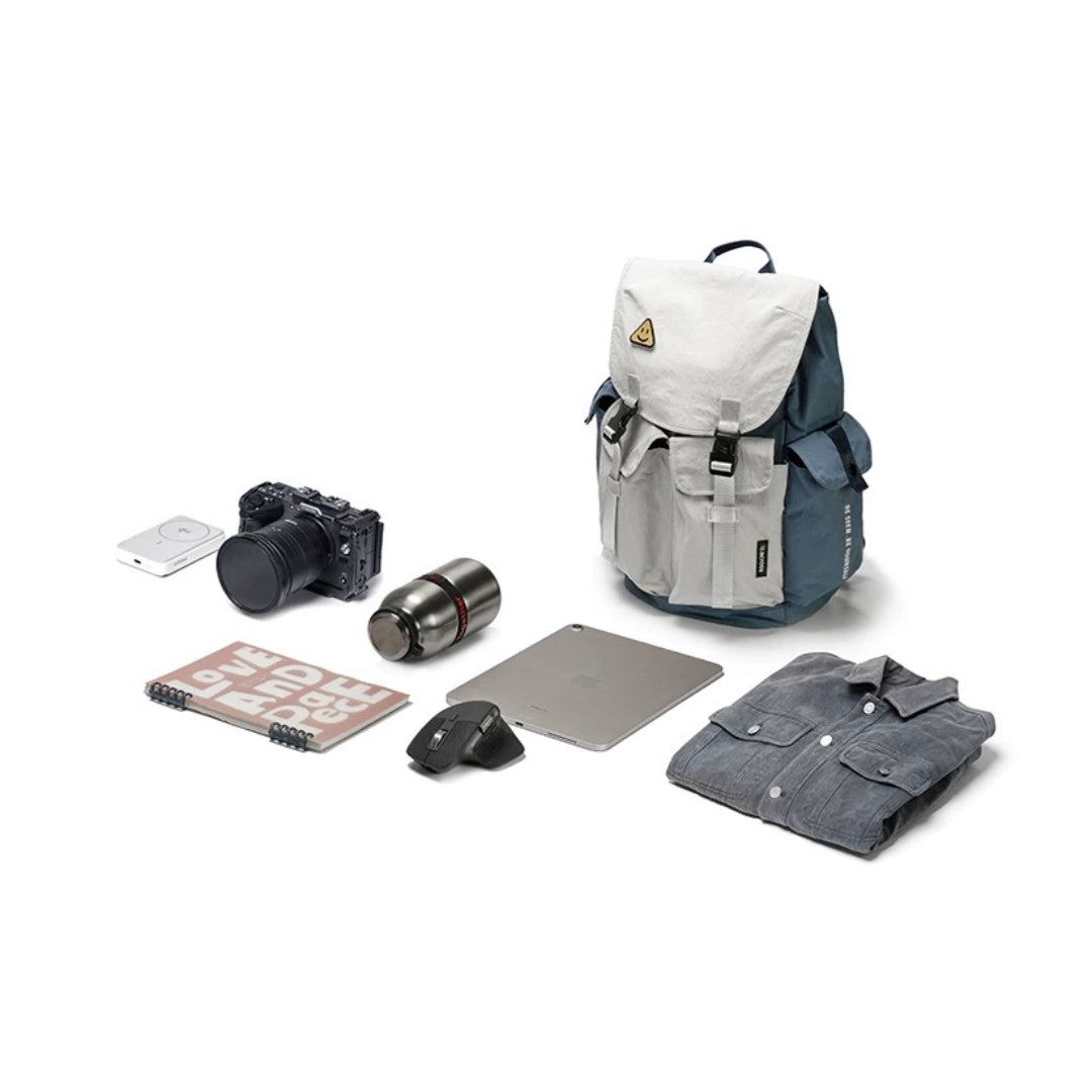 Blue-gray waterproof backpack surrounded by professional gear including camera, laptop, and work essentials for urban professionals
