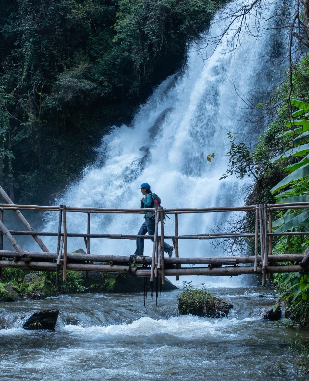 Hiker crossing a bamboo bridge near a waterfall with the 8809 Lightweight Hiking Backpack 19L