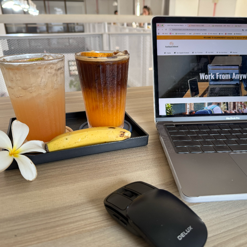 laptop with BackpackBeat website open on desk with drinks representing real digital nomad workspace and work from anywhere setup