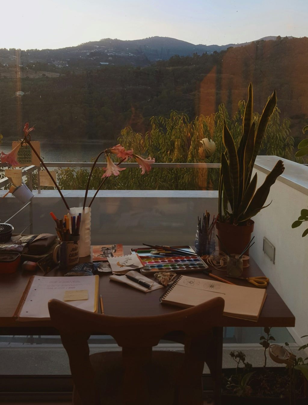 Balcony desk with watercolors, notebooks, and pens set up for freelance work with a mountain view in the background