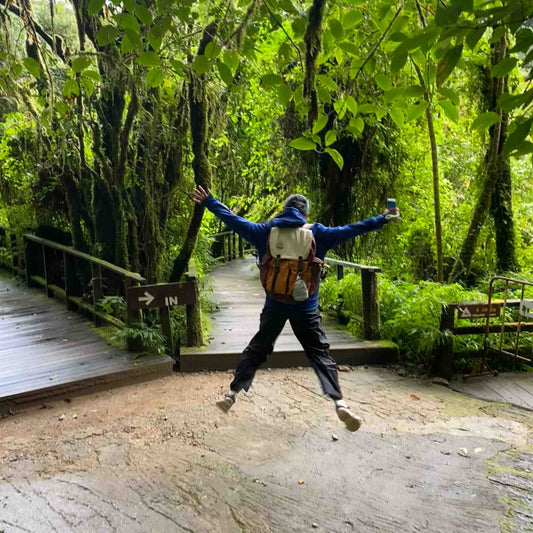 Person wearing Backpackbeat 7706 backpack jumping on wooden pathway in lush green forest, demonstrating lightweight design for outdoor adventures