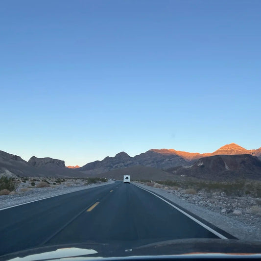 Empty highway through desert mountains at golden hour with RV ahead, representing digital nomad lifestyle constant movement and journey between destinations
