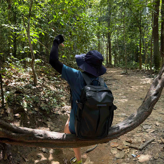 Woman wearing black EXTEND 20L minimalist travel backpack while hiking through tropical jungle trail with dense green foliage