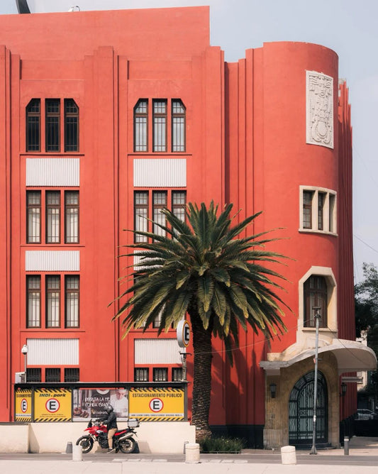 Bright coral-orange Art Deco building in Mexico City with palm tree and parked motorcycle, showcasing vibrant architectural colors in Roma or Condesa district