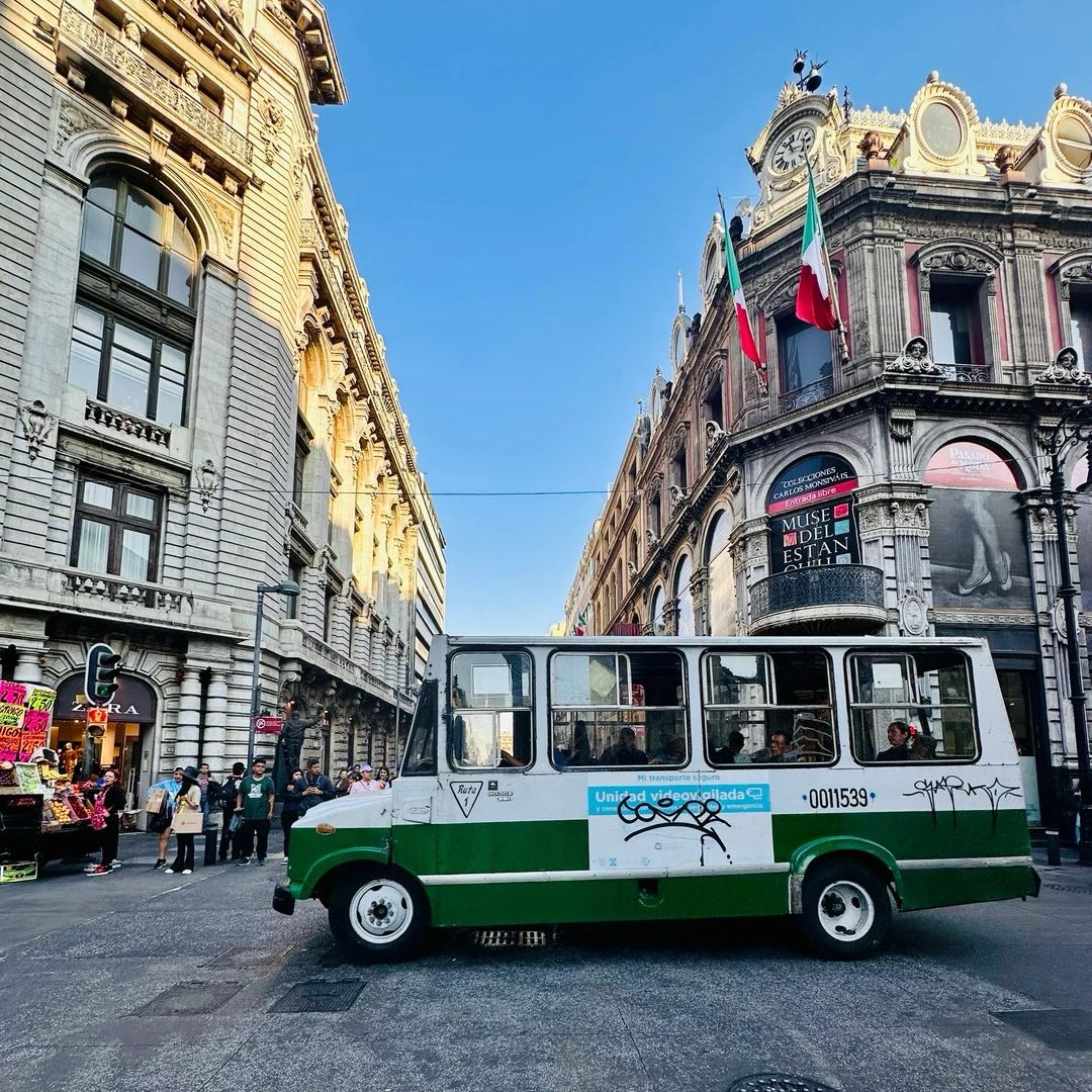 Mexico City downtown street with colonial buildings, Mexican flag, and local green-white bus