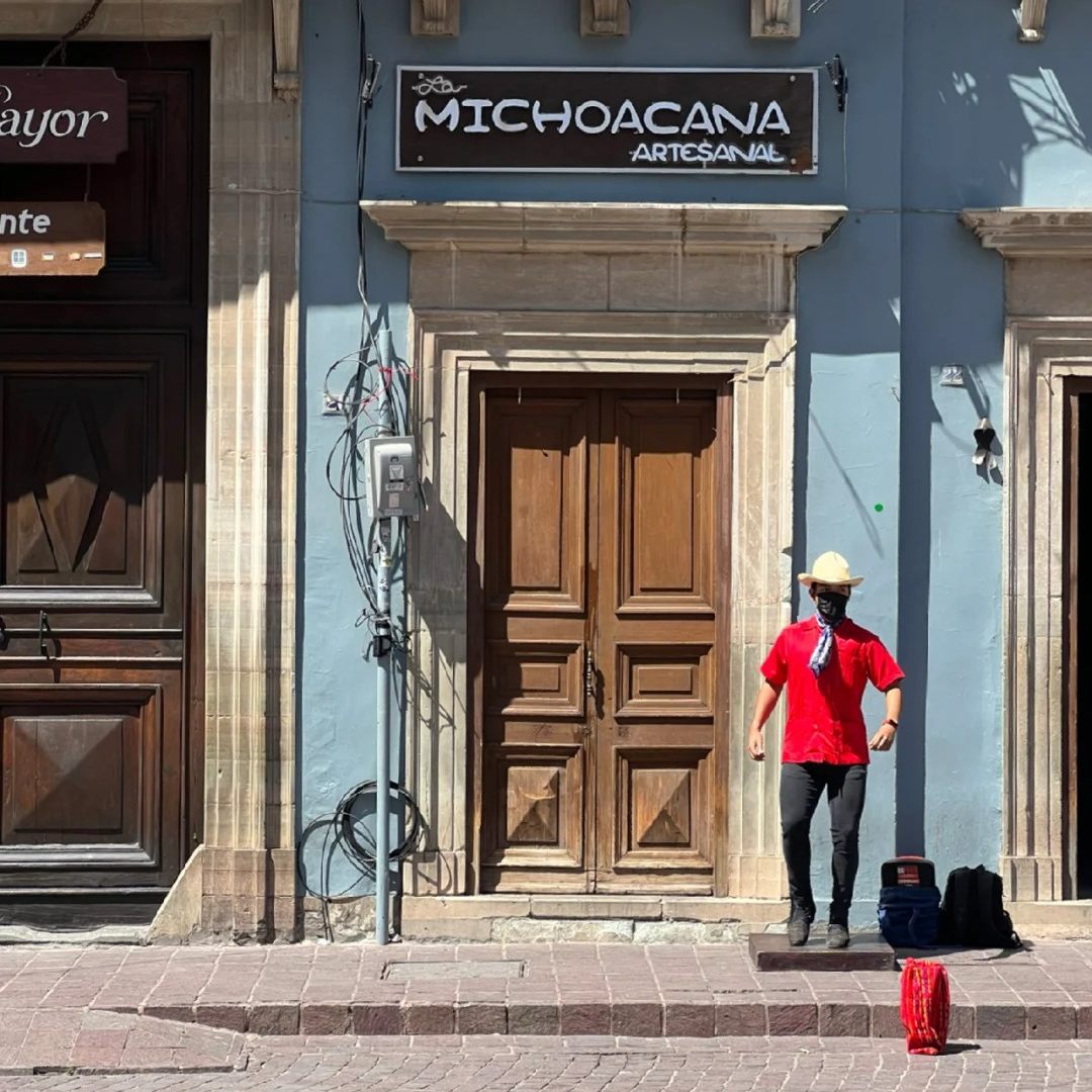 Person walking past blue colonial building in Mexico with wooden door, capturing everyday life of remote workers in stable location
