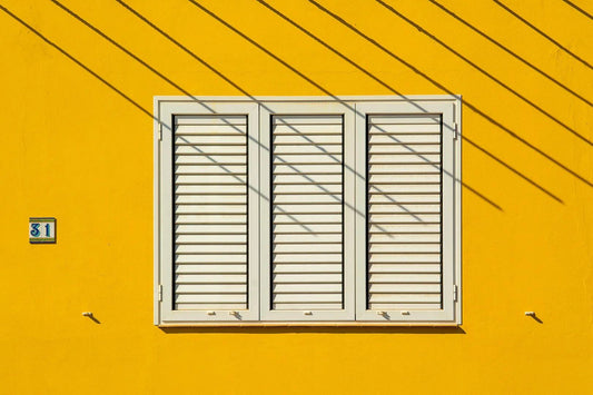 Clean minimalist architecture with yellow wall and white shutters representing design simplicity
