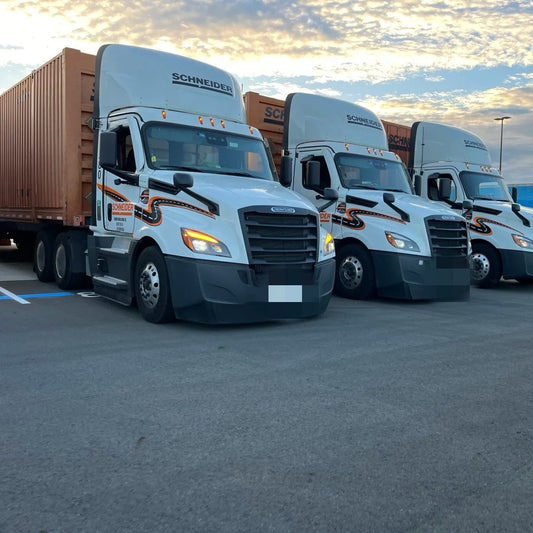 Schneider day cab trucks parked at sunset in a lot.