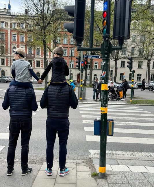 Two modern fathers wearing lightweight backpacks while holding hands with young children crossing city street, demonstrating hands-free parenting and family mobility