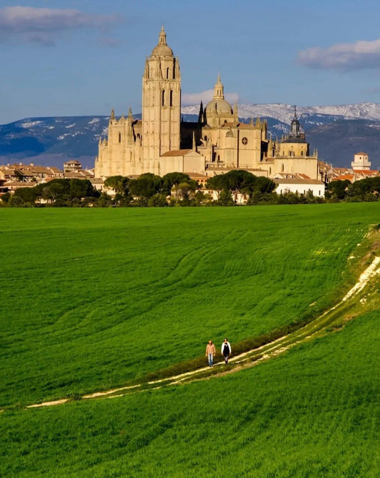 The Alcázar of Segovia rising above green fields under a blue sky