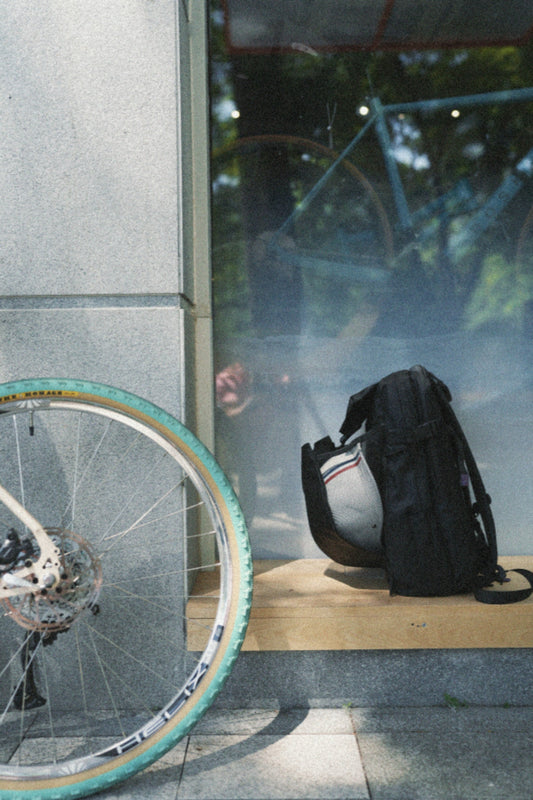 Expandable black backpack resting by a white bicycle on a city sidewalk, ready for a 2-day flexible trip.