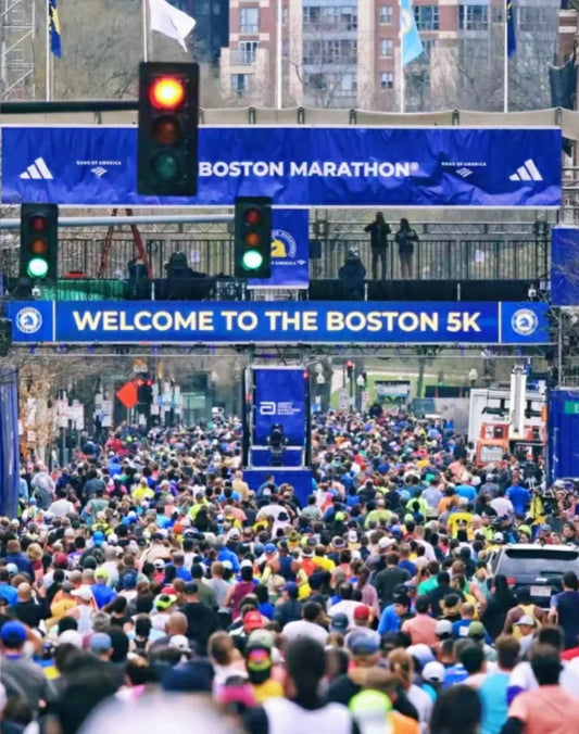 Large crowd at the starting line of the Boston Marathon, with welcome banners and red traffic light overhead.