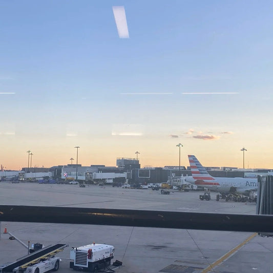 Airport tarmac view with American Airlines plane at gate during sunset, business travelers preparing for departure with carry-on backpacks