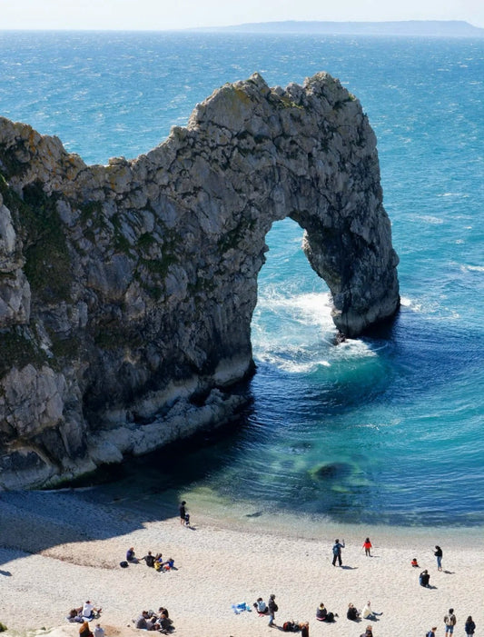 Natural limestone arch of Durdle Door along the Jurassic Coast with people walking on the beach below