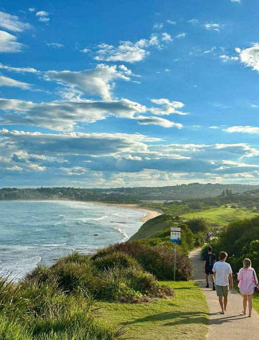 Wooden directional sign pointing toward Long Reef Point and Fishermans Beach, framed by tall trees and blue sky