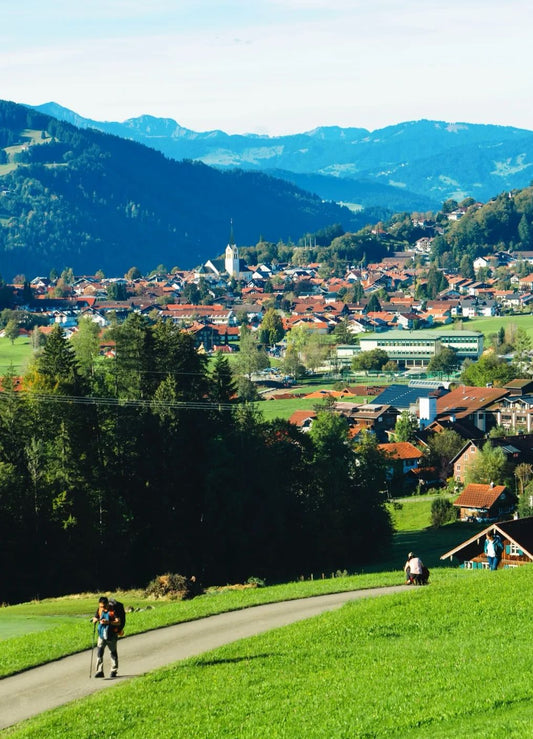 Hiker walking on a paved path with a town and mountains in the background