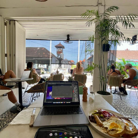 Digital nomads working remotely at Bali coworking cafe with laptops and breakfast - travel gifts essential for this lifestyle
