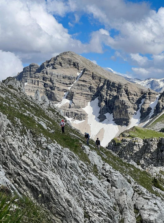 Hikers walking along steep rocky trail with large stone mountain in the background