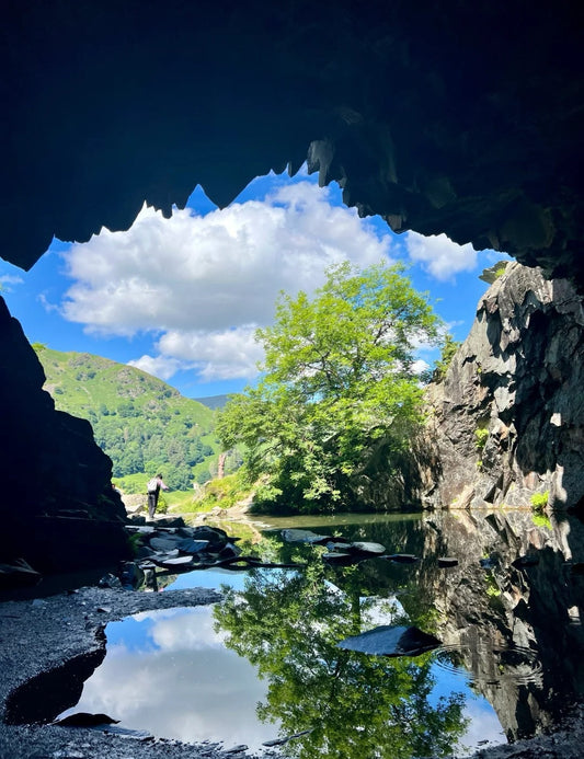 Looking out from inside Rydal Cave towards a reflective lake and lush greenery in the Lake District