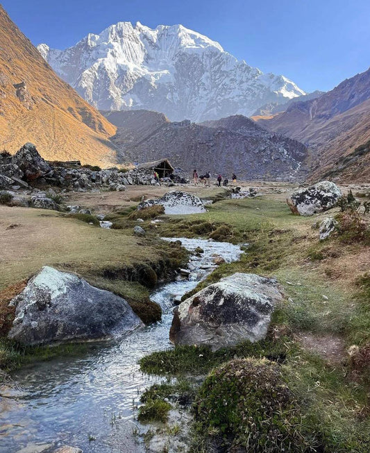 Snow-covered peak and glacial valley with hikers approaching a mountain shelter