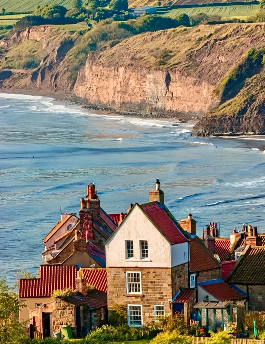 Scenic coastal view of a red-roofed cottage on a cliff above the sea in Whitby