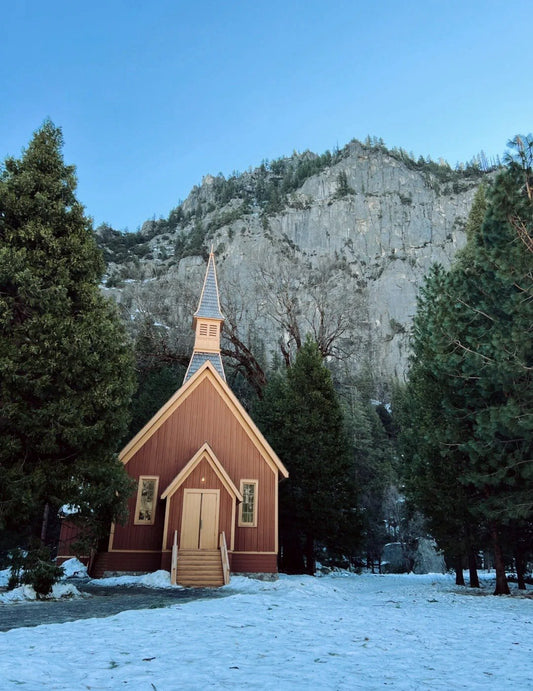 Snow-covered Yosemite Valley Chapel surrounded by tall pine trees on a winter day