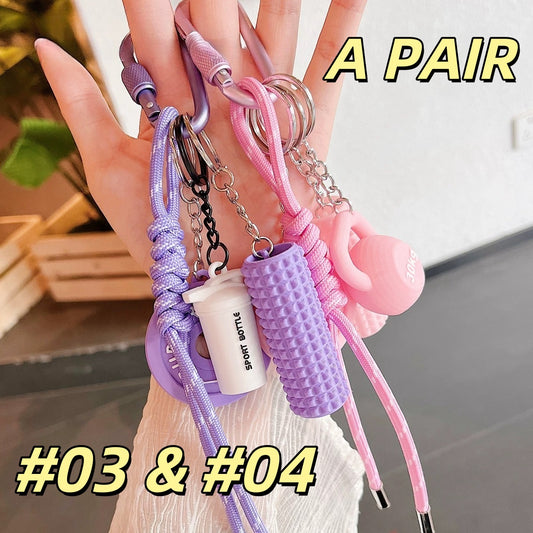 Matching pair of fitness keychains AC#03 and AC#04 in pink and purple, displaying BURGER FITNESS weight plates, dumbbells, and foam rollers with Sport Bottle tags