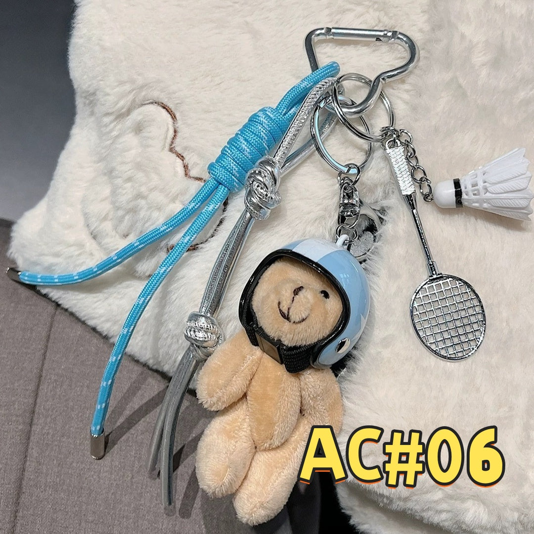 Blue sports keychain AC#06 featuring teddy bear with blue cap/headphones and detailed tennis racket charm with braided cord attachment