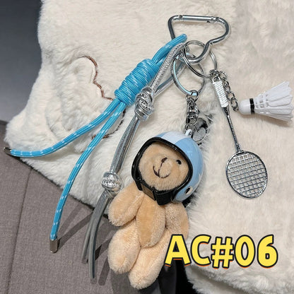 Blue sports keychain AC#06 featuring teddy bear with blue cap/headphones and detailed tennis racket charm with braided cord attachment