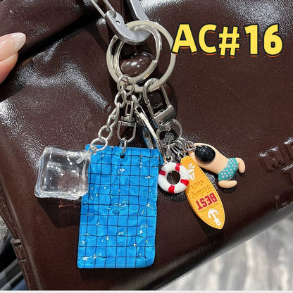 Blue swimming pool keychain AC#16 with mosaic tile pattern, swimmer figure, red and white life ring, Best card, and clear acrylic cube charm