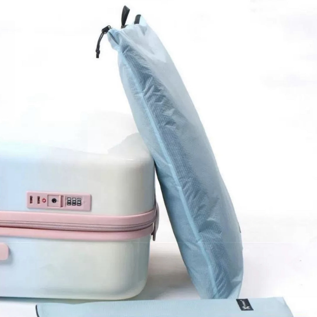Light blue BackpackBeat waterproof wet dry bag standing upright next to white and pink suitcase showing slim foldable design