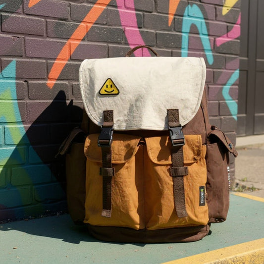 A vibrant street art alley during a sunny day. The Backpackbeat backpack is placed on a clean, colorful section of pavement next to a brightly painted mural. Sunlight illuminates the intricate details of the artwork and the backpack. The alley is tidy and inviting, with no people, emphasizing the urban environment.