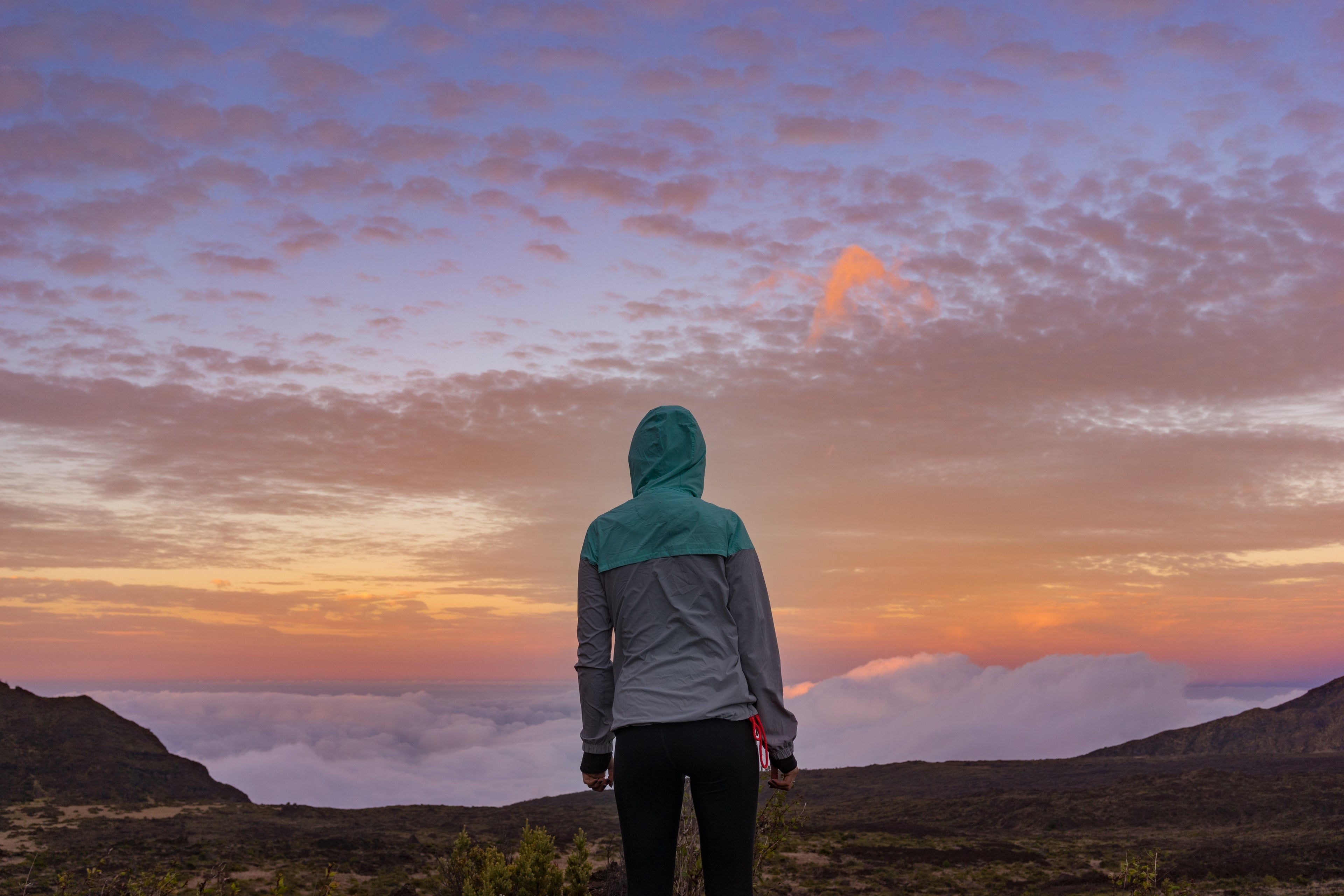 A woman in a hooded jacket standing on a mountain at sunset, reflecting BackpackBeat’s spirit of mindful adventure and outdoor freedom.